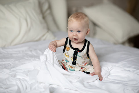 A young baby wearing happy dumpling pajamas is playning with a blanket