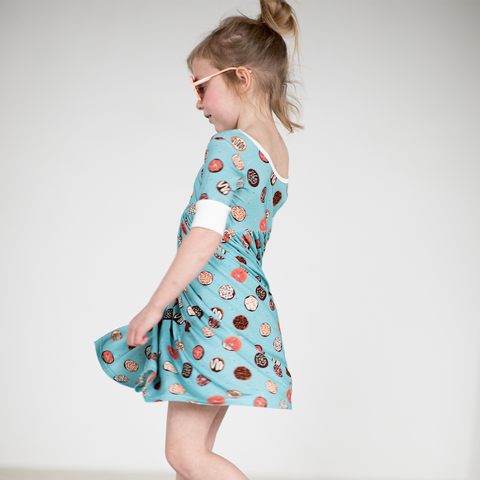 A girl is twirling in a colorful flowy donut print dress. She also has on pink sunglasses! 